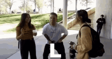 a man and two women are standing next to each other on a sidewalk in front of a building .