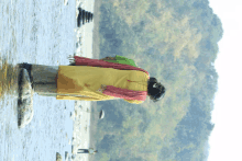 a woman in a yellow coat and red scarf stands in a river