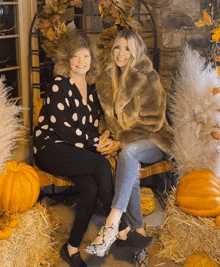 two women sitting next to each other in front of pumpkins and hay