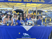 a group of people sitting at a table under a rams republic banner