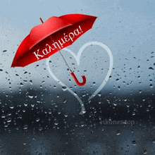 a red umbrella with the word kalimera written on it is sitting on a window with rain drops .