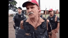 a man with a mustache wearing a red hat and a name tag that says joao is talking to a group of men