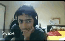 a young man wearing headphones is sitting in a bedroom with his hand on his chin .