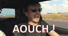 a man wearing sunglasses is driving a car and the word aouch is on the bottom