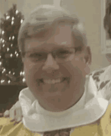 a man wearing glasses and a yellow robe is smiling .