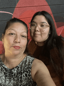 two women pose for a picture in front of a red wall