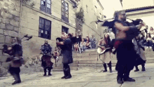 a group of people dressed in medieval costumes are dancing in front of a crowd of people sitting on stairs .