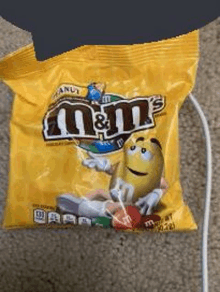 a bag of m & m 's candy is sitting on a carpet next to a cord .