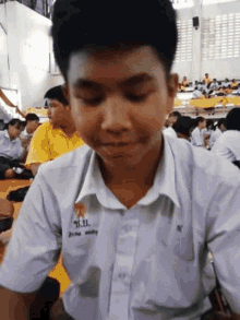 a boy in a school uniform is sitting at a table with his eyes closed in a crowded room .