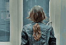 a woman in a leather jacket is walking through a doorway .