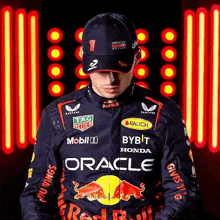 a man in a red bull racing suit and hat is standing in front of a red light .