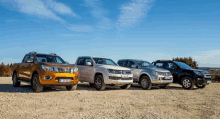 four pickup trucks are parked in a row on a dirt road .