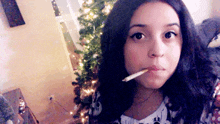 a woman is smoking a cigarette in front of a christmas tree .