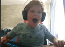 a young boy wearing headphones is making a funny face while sitting at a desk .