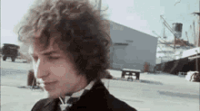 a man with curly hair is standing in front of a building in a parking lot .