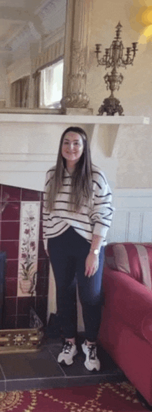 a woman in a striped sweater is standing in a living room in front of a fireplace .