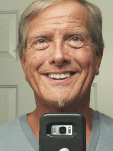 a man smiles while taking a picture of himself with a cell phone