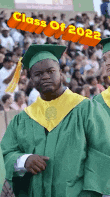 a man in a graduation cap and gown is standing in front of a crowd with the words class of 2022 written above him