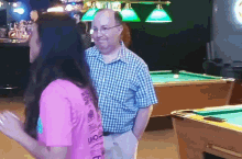 a man and a woman are standing in front of a pool table and the woman is wearing a pink shirt that says i love you