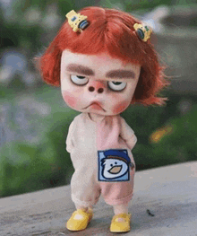 a doll with red hair is standing on a wooden table with her eyes closed .