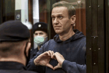 a man making a heart shape with his hands in front of a window