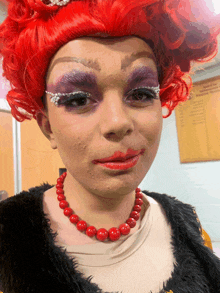 a woman wearing a red wig and a red necklace is standing in front of a bulletin board