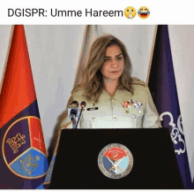 a woman in a military uniform stands behind a podium with flags behind her