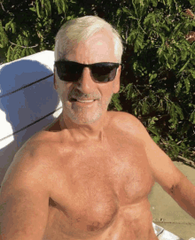 a shirtless man wearing sunglasses is sitting on a white chair