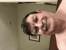 a shirtless man with a mustache is smiling in front of a framed picture