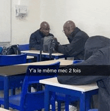 a group of men are sitting at desks in a classroom talking .