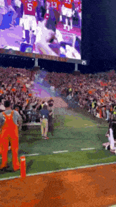 a man in orange overalls stands on a football field in front of a large screen that says clemson on it