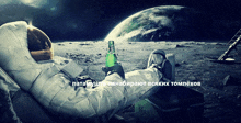 an astronaut is laying on the moon holding a green bottle of beer