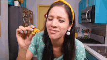 a woman in a green shirt is eating a piece of food in a kitchen with a microwave and refrigerator in the background