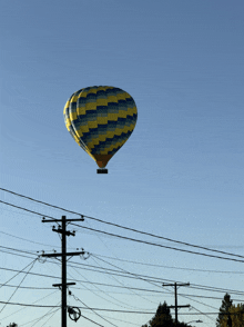 a blue and yellow hot air balloon is flying over a telephone pole