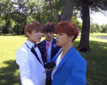 three young men in suits are standing next to each other in a park with trees in the background .