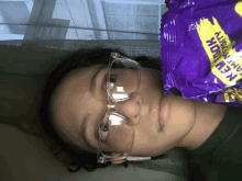 a woman wearing glasses holds a purple bag that says ' new ' on it