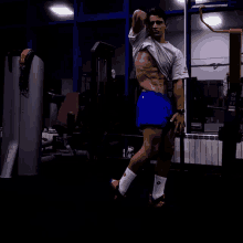 a man in a white shirt and blue shorts stands in a dark gym