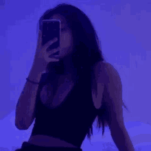 a woman in a black tank top is taking a selfie with her phone .