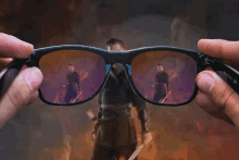 a person is holding a pair of glasses with a reflection of a man holding a sword in the lenses