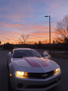 a silver car with a red stripe on the side is parked in a parking lot at sunset