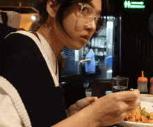 a woman wearing glasses sits at a table with a plate of food