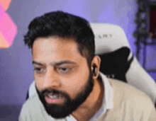 a man with a beard is sitting in a chair and looking at the camera .