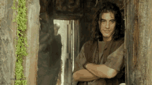 a man with long hair is standing in a doorway with his arms crossed and smiling