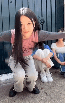 a girl with long hair is sitting on the ground with her arms outstretched next to two other girls .