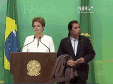 a man in a suit stands next to a woman at a podium with the word brasil on the screen behind them