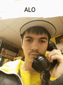 a man wearing a hat is talking on a telephone and the word alo is above him