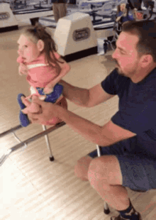 a man is kneeling down next to a little girl in a bowling alley with a bowling alley sign in the background