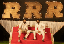 two men sit on a red staircase in front of a sign that says rrr