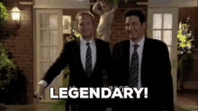 two men in suits and ties are standing in front of a brick building and one of them is pointing at the word legendary .