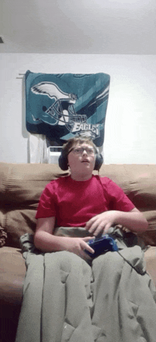 a boy wearing headphones is sitting on a couch with a philadelphia eagles blanket behind him